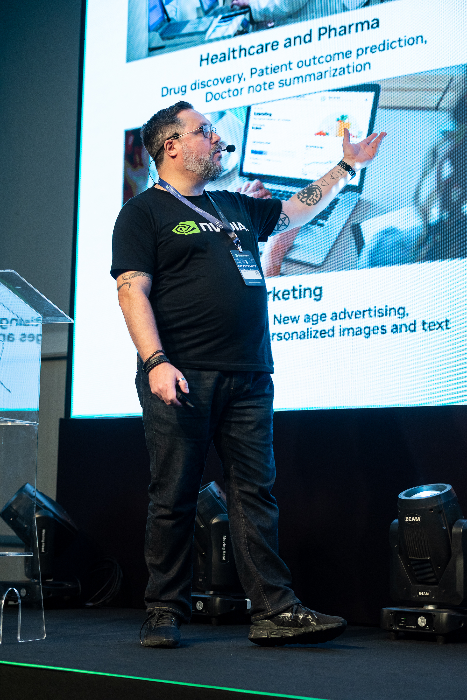 Na fotografia, Jomar aparece no palco, com calça e camiseta preta e, ao fundo, seu slide