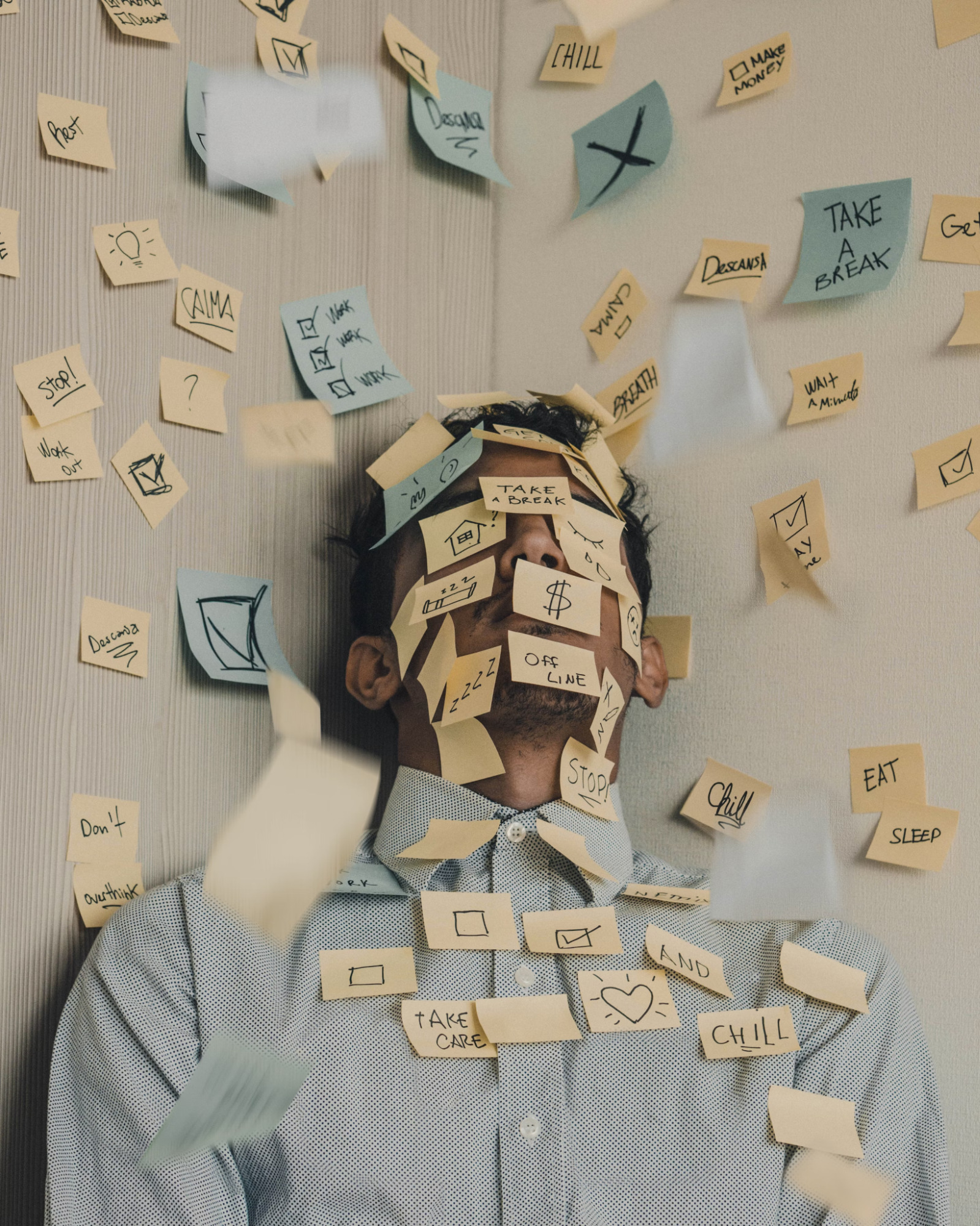 Homem branco vestindo camisa em tom azul cercado de diversos post-its com tarefas a serem realizadas.