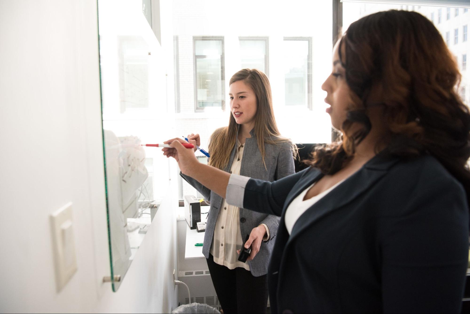 Foto de duas mulheres conversando e fazendo anotações em um quadro à frente delas.