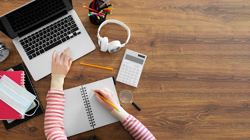 Mulher estudando através do computador e fazendo anotação no caderno.