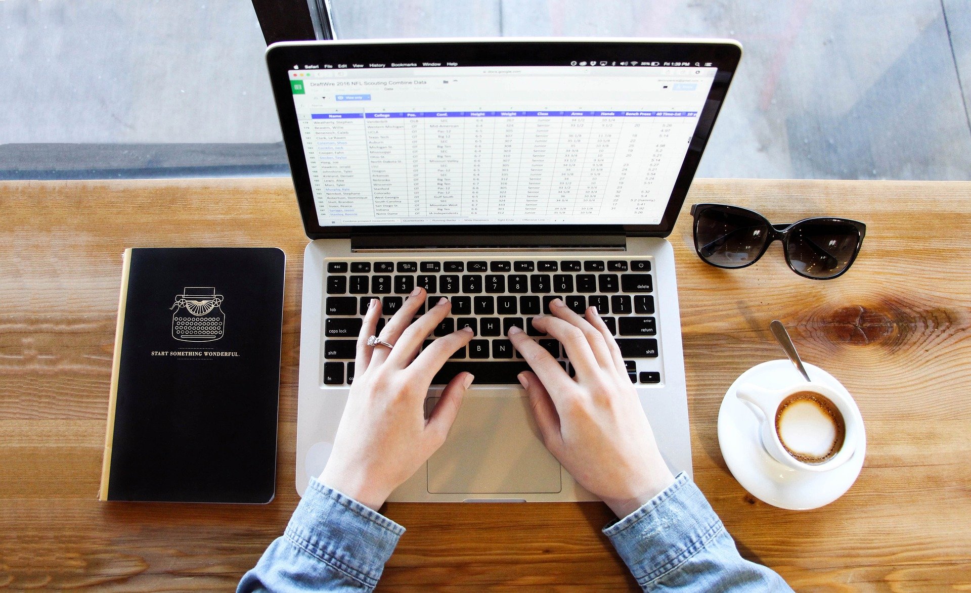 Mesa com óculos preto, xícara de café com café e um notebook.